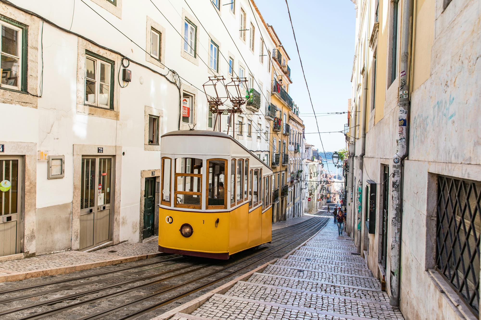 White and yellow train car going through the streets of Lisbon